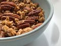 Close-up of a bowl filled with granola and pecans on a white surface