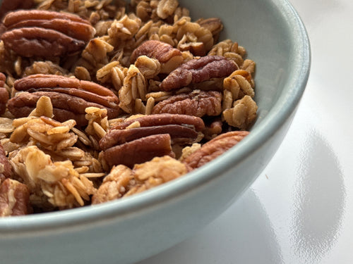 Close-up of a bowl filled with granola and pecans on a white surface